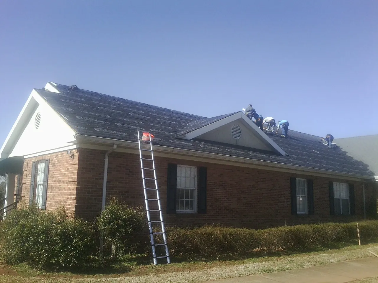 Crew tearing shingles off a brick ranch roof with a ladder set — Metal Roof Repair work by our crew in Vermillion