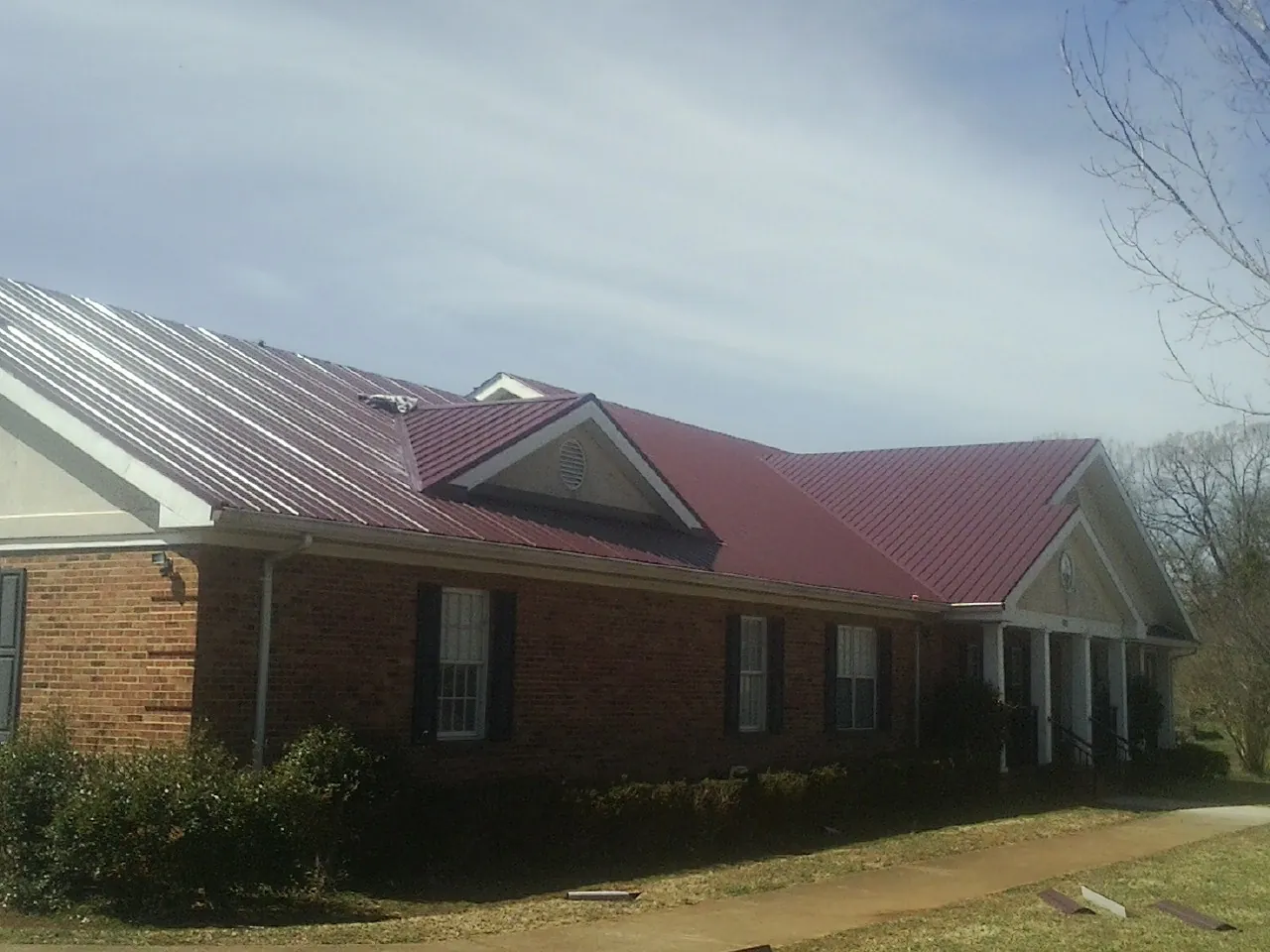 Red metal roof with gabled entries on a long brick building, from a Hail Damage Roof Repair job in Vermillion