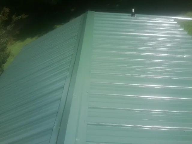 New green metal panels meeting at the ridge of a roof — Flat Roof Repair work by our crew in Vermillion