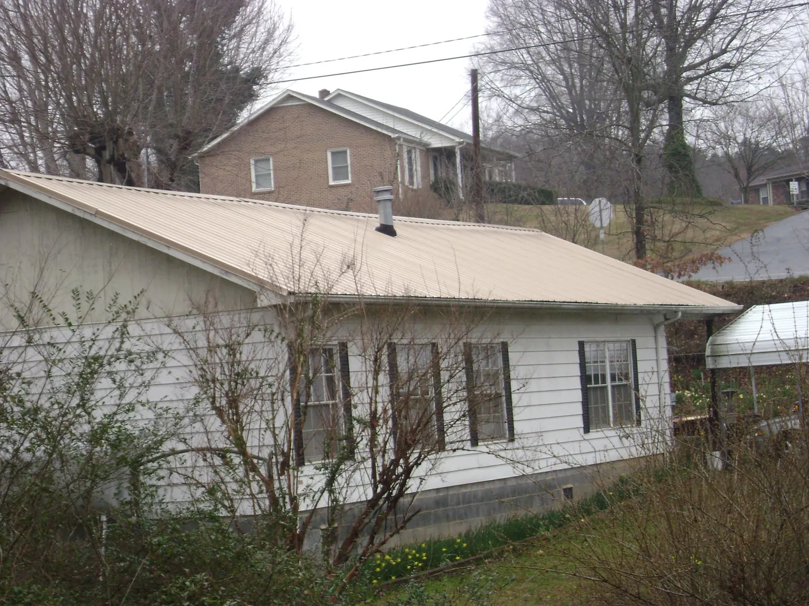 Tan metal roof on a white sided house set into a hillside — Commercial Roofing by Roofing Brothers in Vermillion